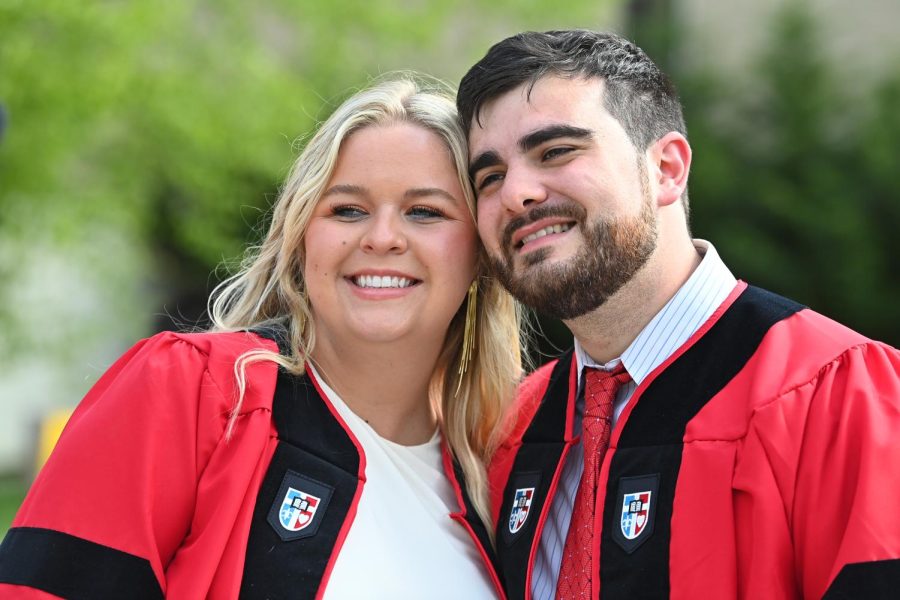 St. Johns Law alumni Ashlyn Stone and Matthew Pate, wearing red and black graduation gowns, smile with their heads leaning together.
