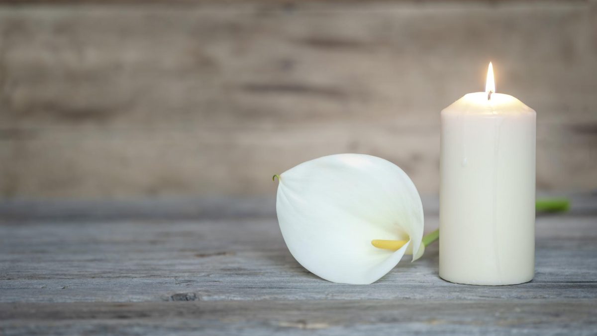 A flower and a burning candle in front of a wooden background.
